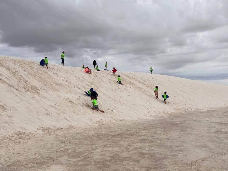 A group of people are sledding down a sand dune.