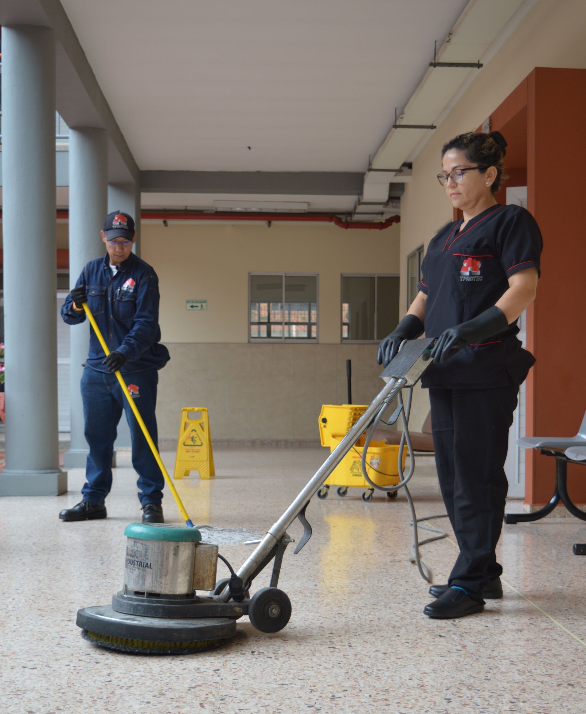Un hombre y una mujer están limpiando un piso con una máquina.