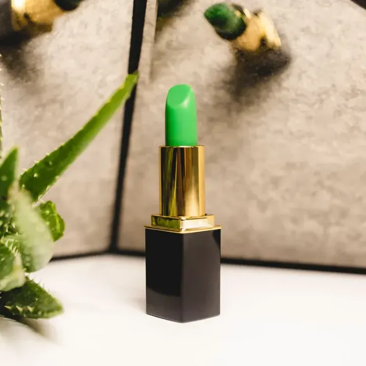 Bright green lipstick in a gold tube on a black base, standing on a white surface.
