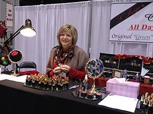 Vendor smiling behind display table at trade show booth with colorful items and banner.