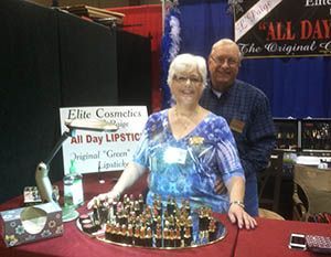 Couple at a cosmetics booth with rows of lipsticks and a sign reading “All Day Lipstick.”