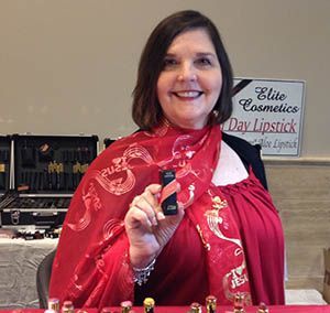 Smiling woman in red scarf holds lipstick at a cosmetics display table