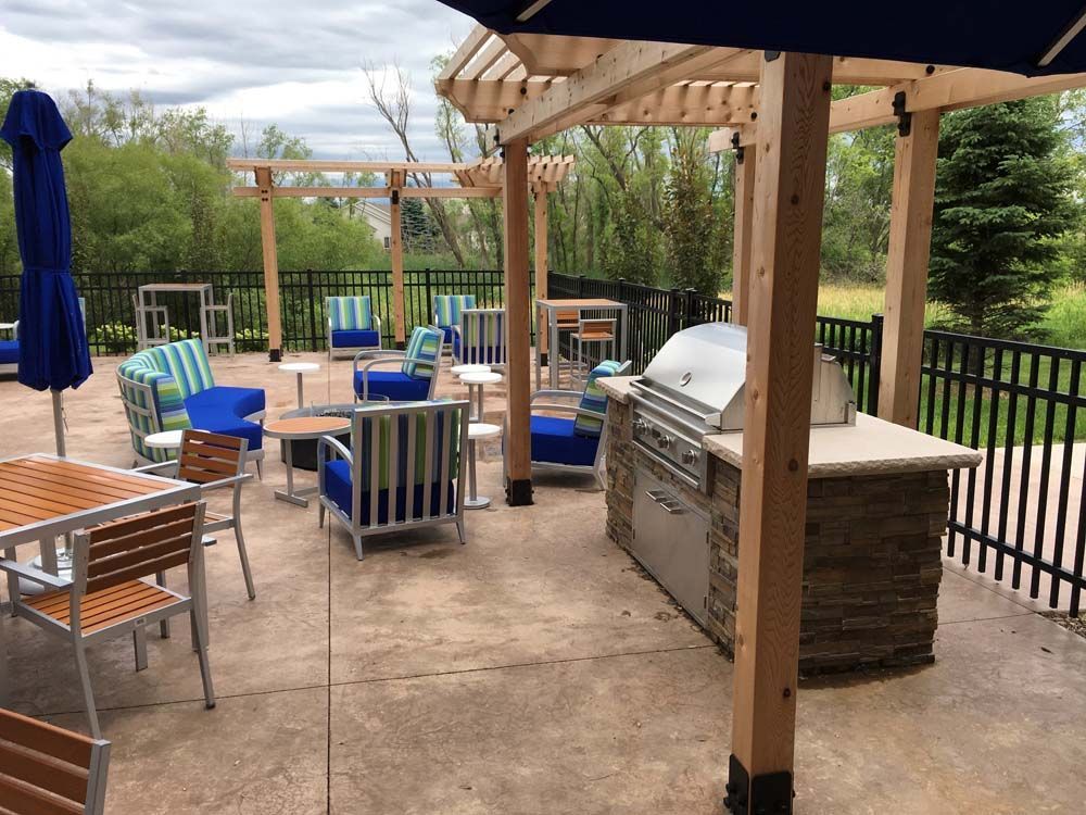 Outdoor patio with seating, tables, and grill under a wooden pergola. Blue, green, and white accents.