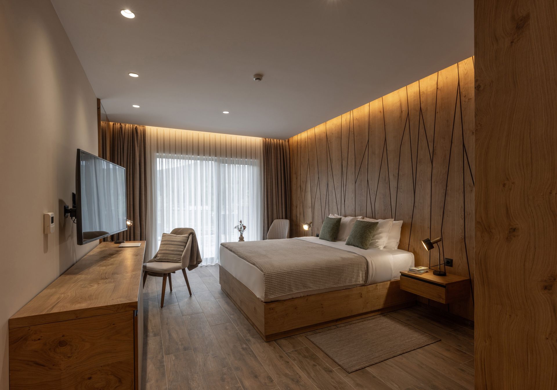 Modern hotel bedroom with wooden accents, bed, TV, and window.