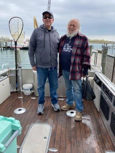 Two men on a boat dock, one in a jacket and hat, the other in a plaid shirt.