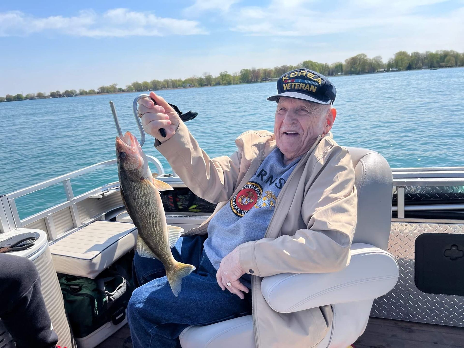 Man on a boat, holding up a fish he caught. Blue water and sky, sunny day. He is smiling.