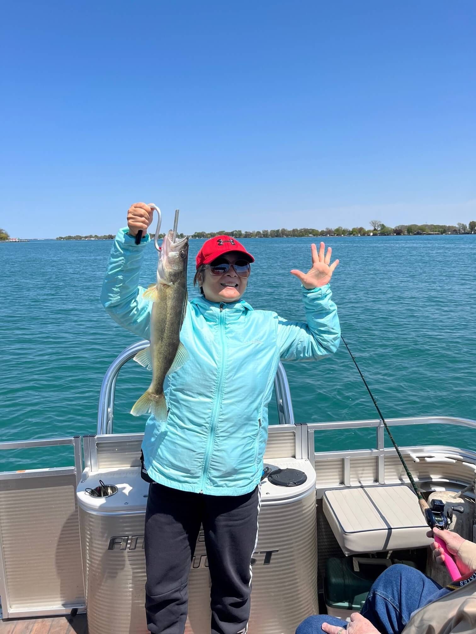 Person on a boat holding up a fish, smiling. Clear blue water and sky.