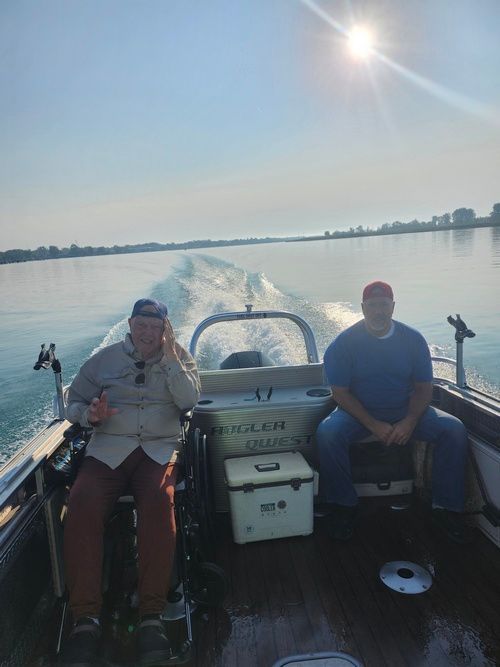 Two men in a boat on water under a bright sun. One man gives a thumbs-up.