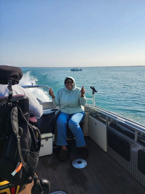 Person on boat, smiling, gives thumbs up, riding on water. Clear sky.