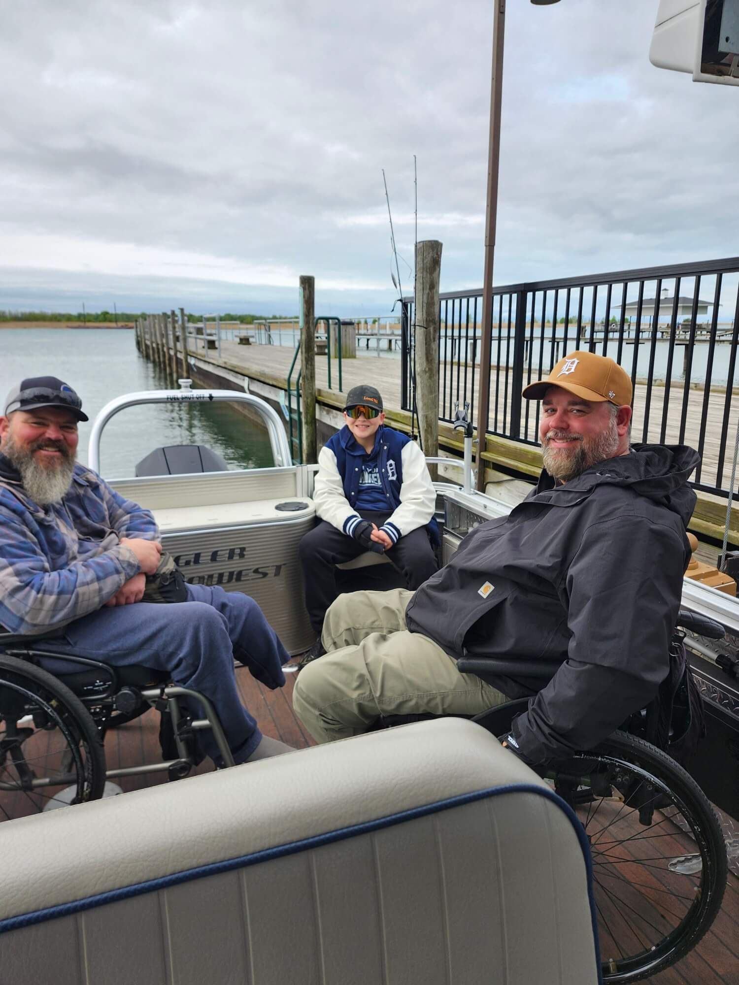 Three people in wheelchairs chatting on a waterfront deck by the harbor.