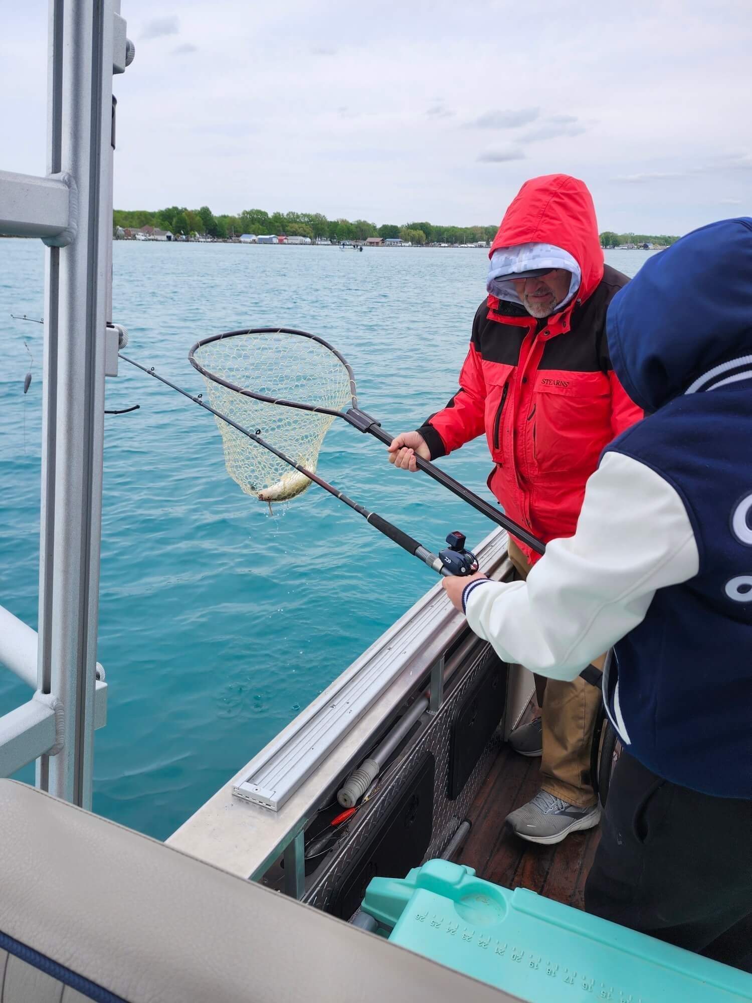 Two people in jackets use a net to catch something from a boat on turquoise water.