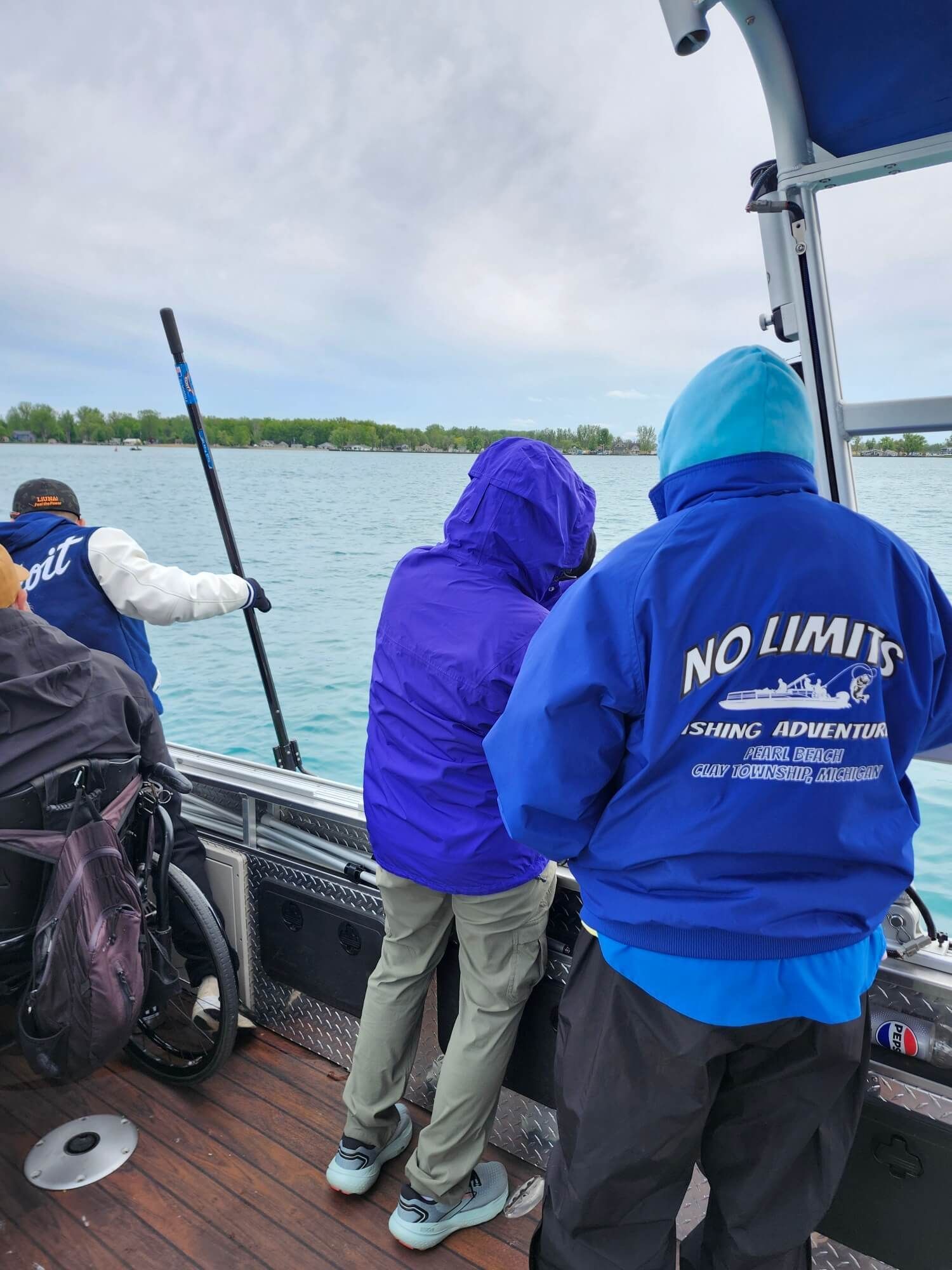 People on a boat wearing blue hoodies, looking out over a calm lake under cloudy skies