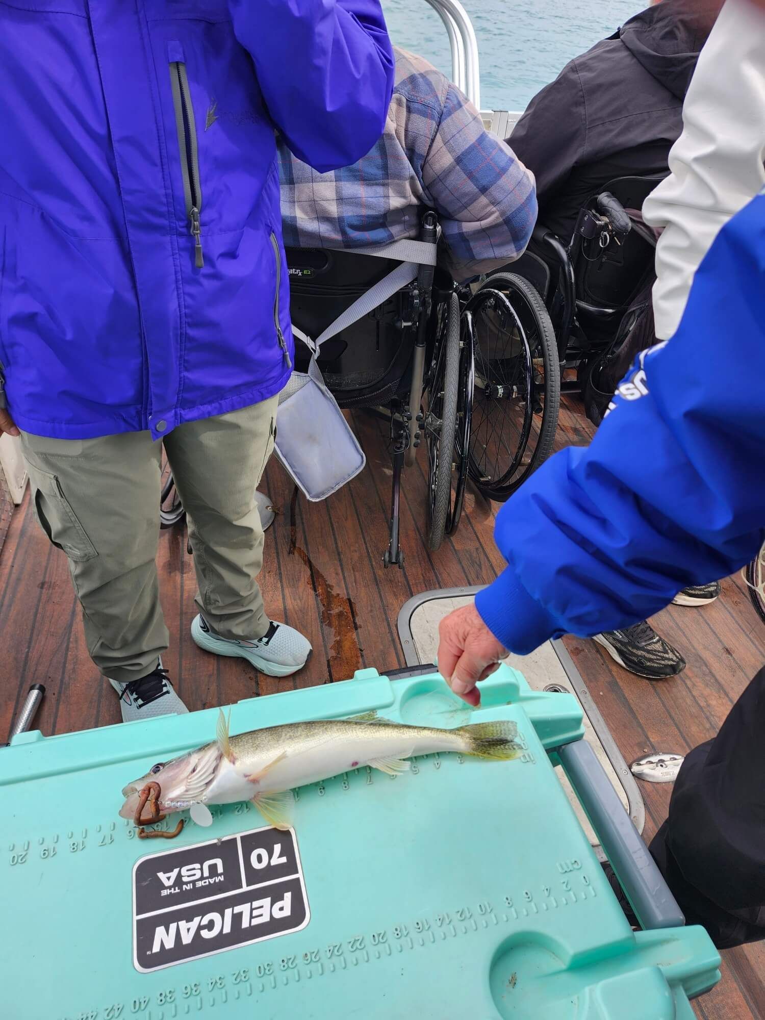 Seafood on a turquoise tray at an outdoor fish market, with people standing nearby on a wooden deck.