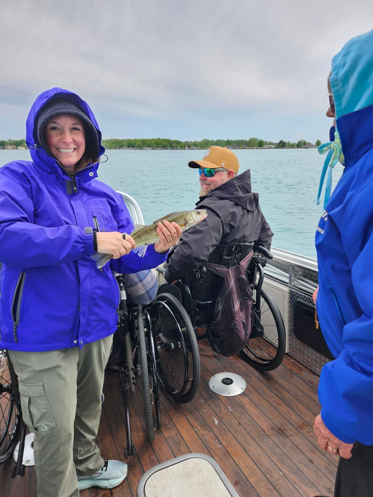 People in rain jackets on a boat, smiling and preparing to fish on calm water