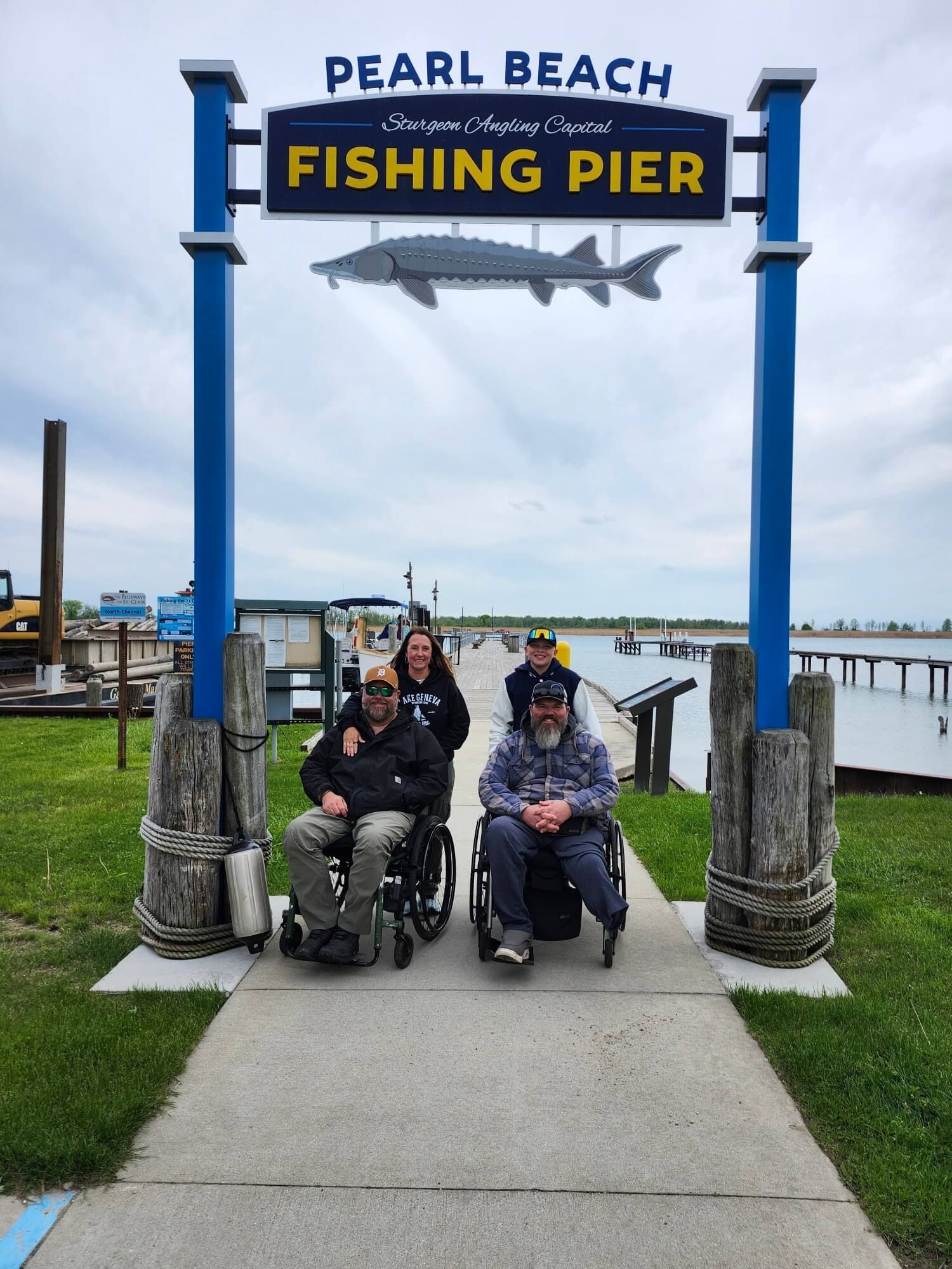 Pearl Beach Fishing Pier sign over three people seated on a path by the water