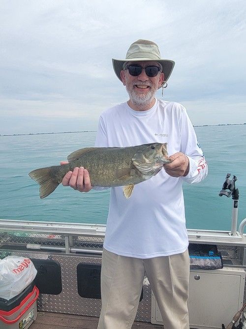 Man on boat holding up a fish, ocean background.