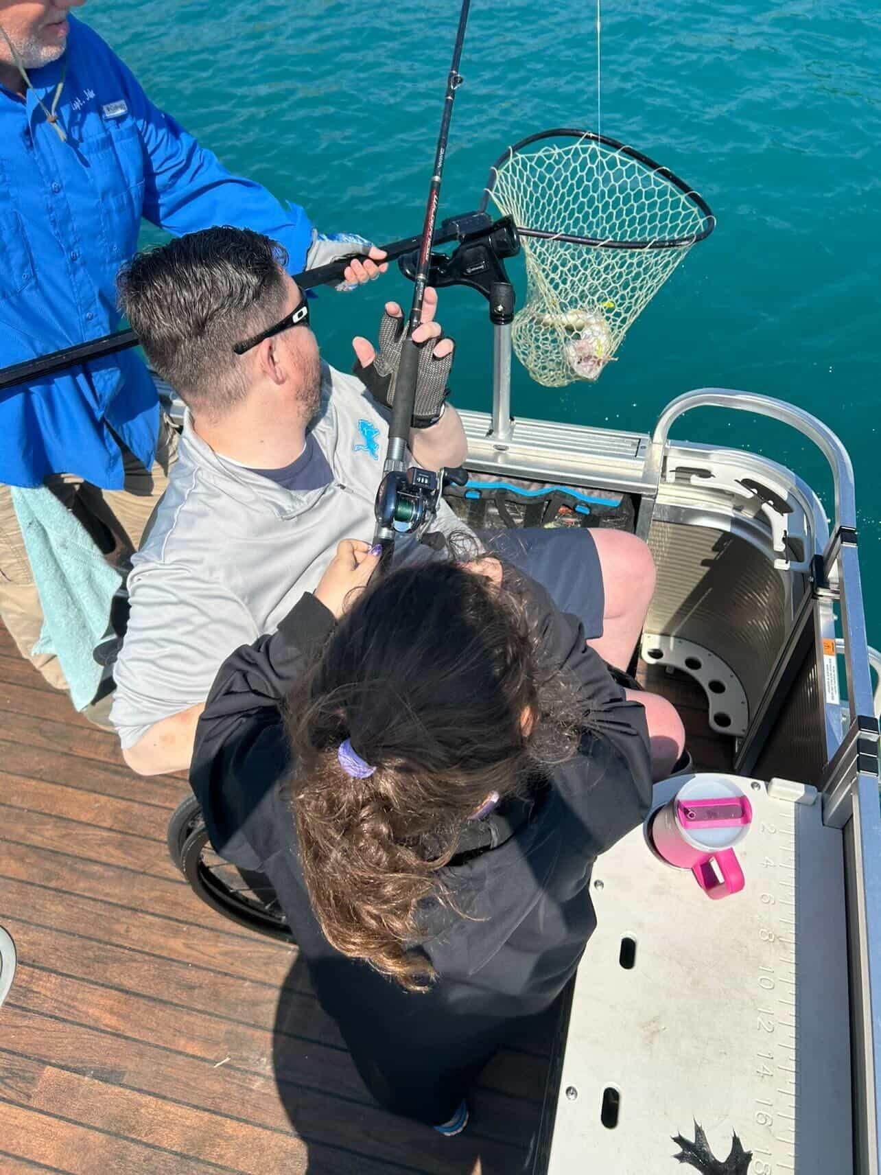Three people on a boat hoist a fishing net over teal water.