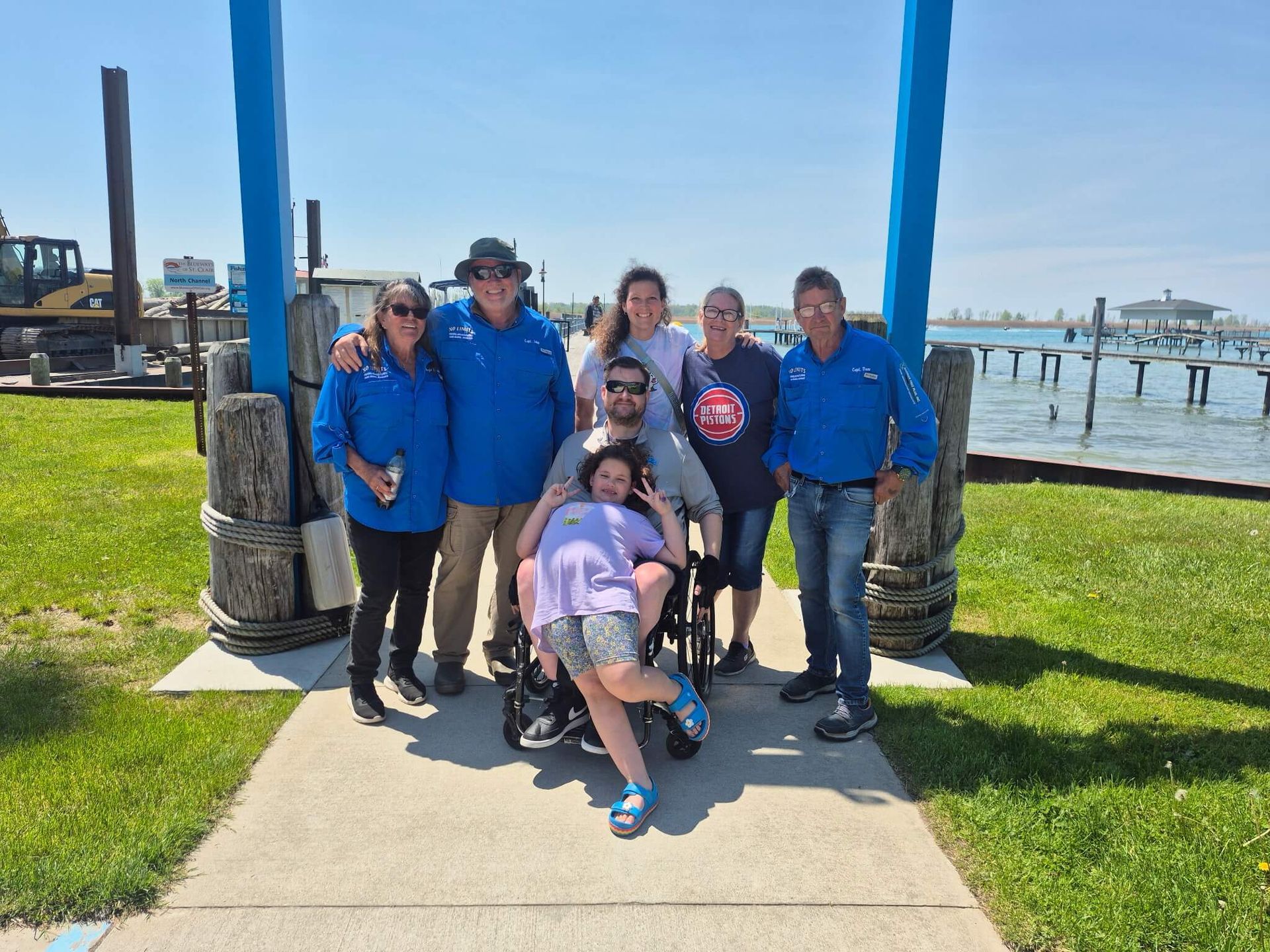 Group in blue jackets posing on a sunny waterfront walkway near a dock.