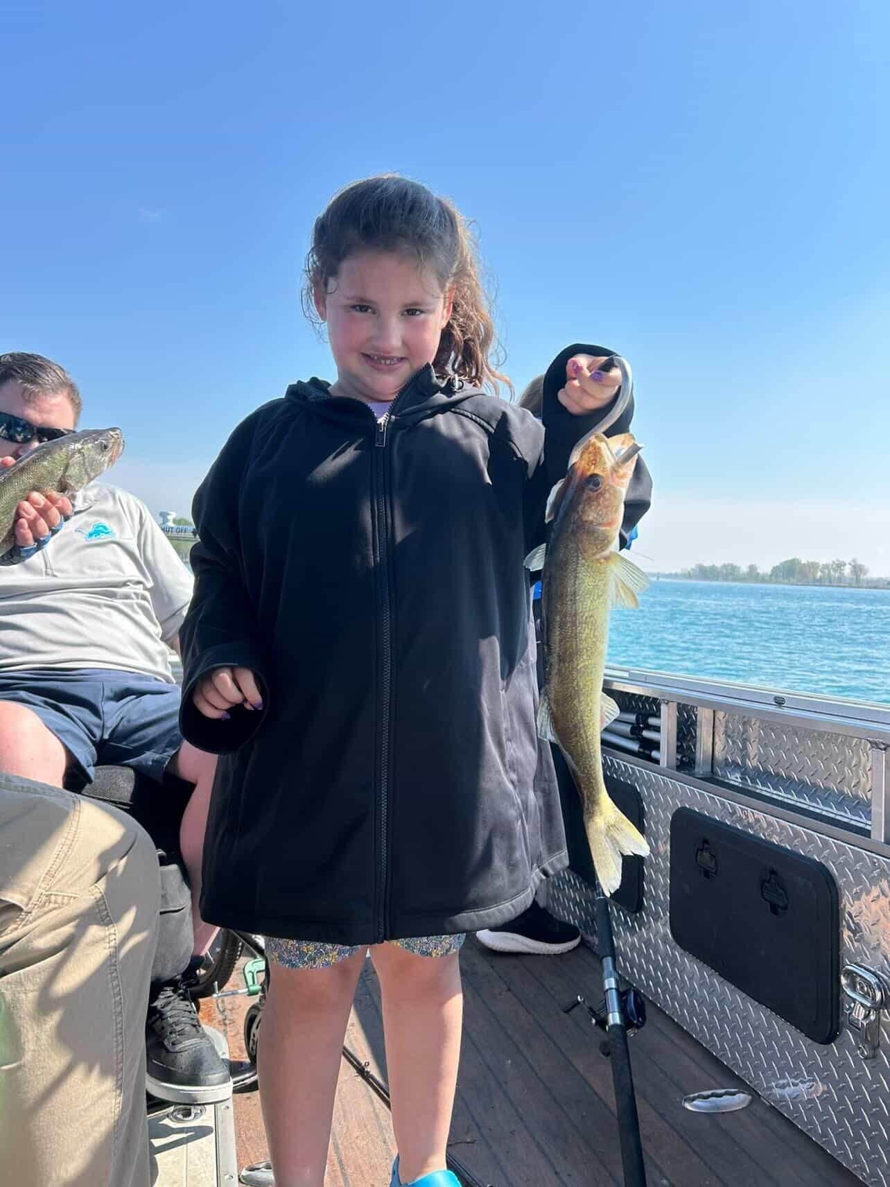 Child on a boat holds up a fish beside calm blue water on a sunny day
