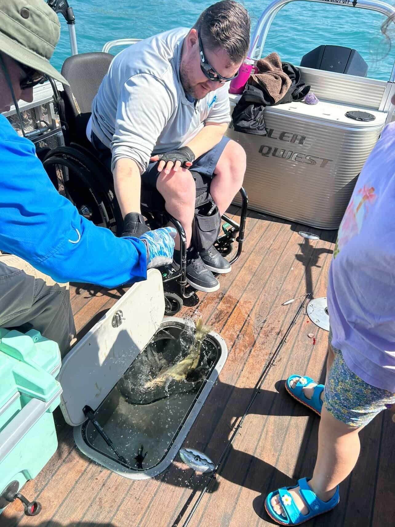 People on a boat handle a large fish on a wooden deck near the water.