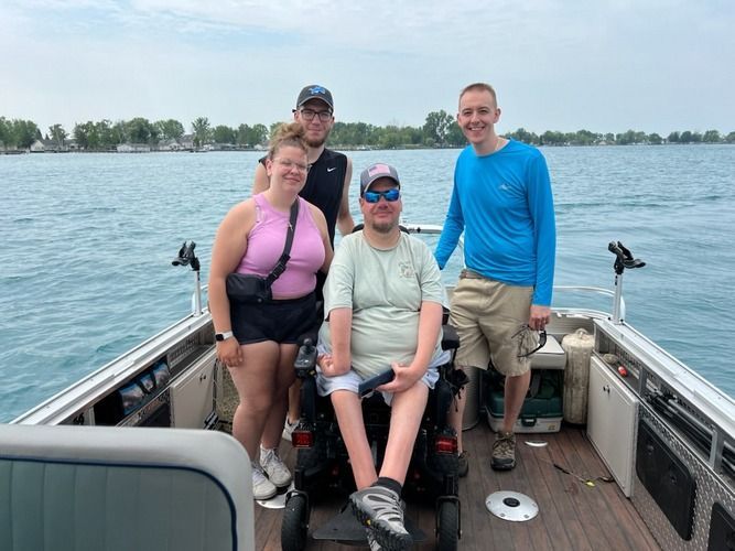 Four people on a boat, one in a wheelchair, smiling at the camera on a body of water.