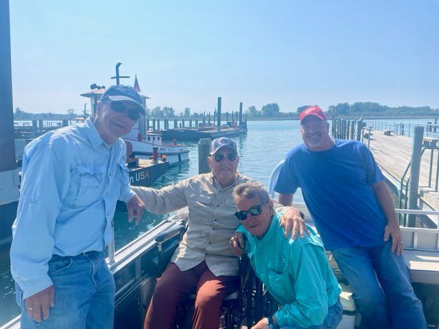 Four men on a boat dock, posing for photo on a sunny day.