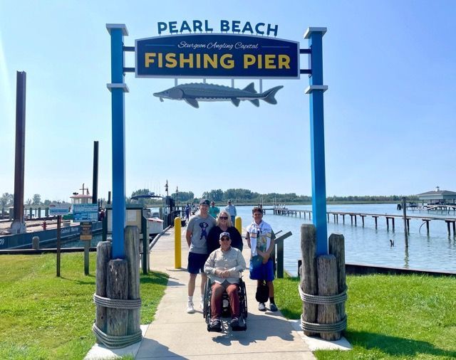 Group near Pearl Beach Fishing Pier archway, one in a wheelchair, sunny day.
