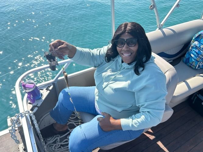 Woman on boat holding up a small fish, smiling, near blue water.