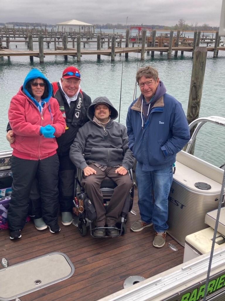 Four people on a boat near a dock. One is in a wheelchair. They are bundled in jackets, preparing for a trip.