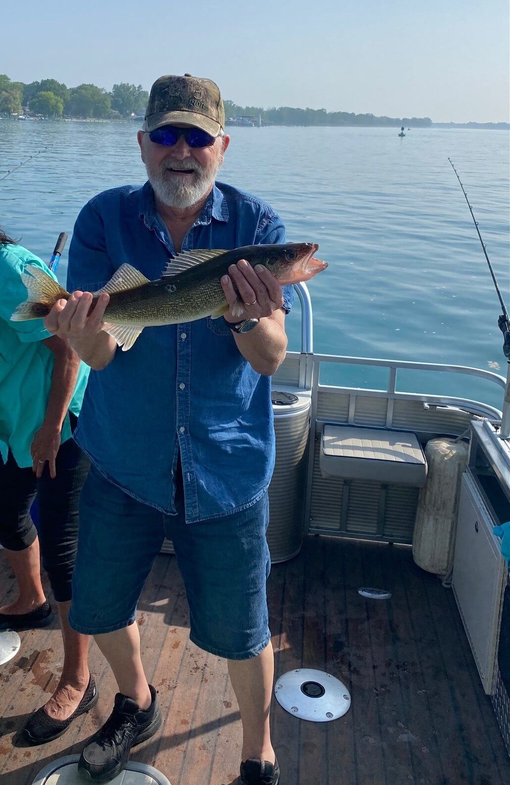 Man on boat holding fish, blue water background.