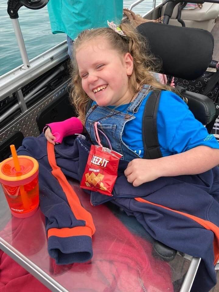 Smiling child in overalls on a boat, holding a snack and drink.