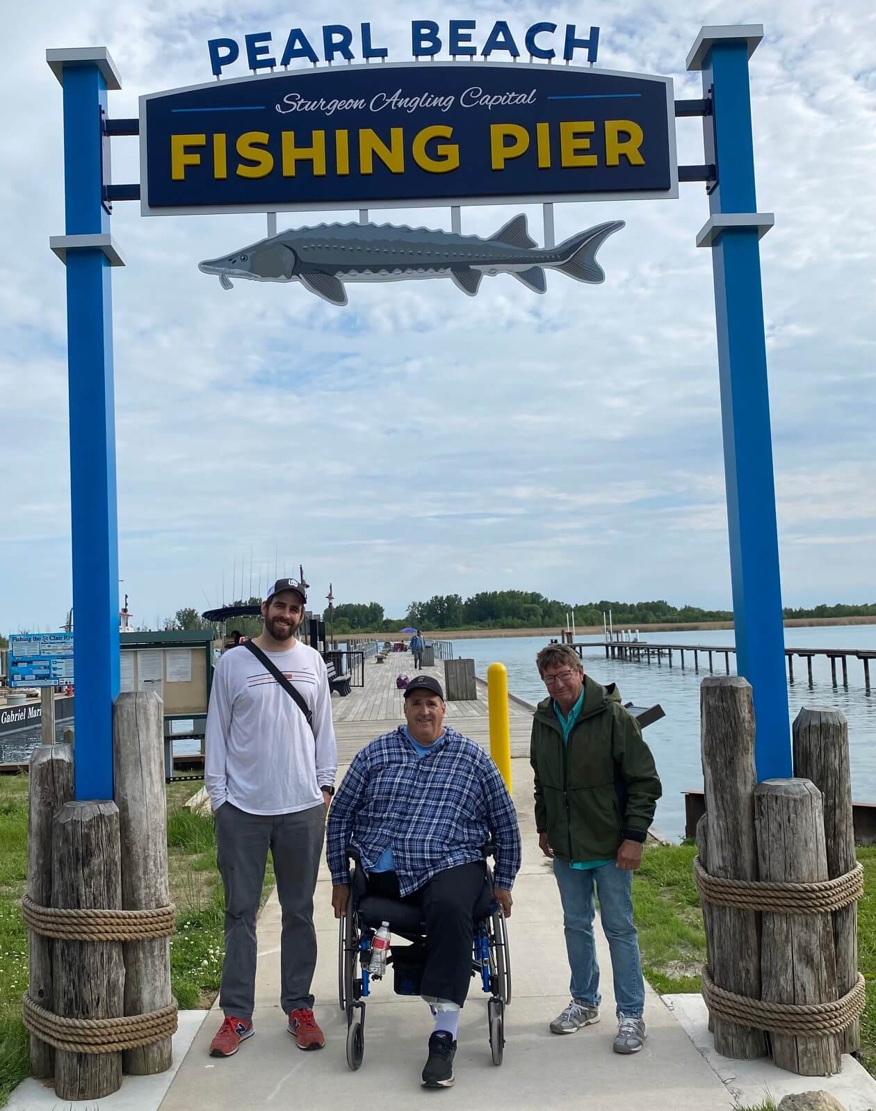 Three people at the Pearl Beach Fishing Pier. One is in a wheelchair. A sign features a fish.