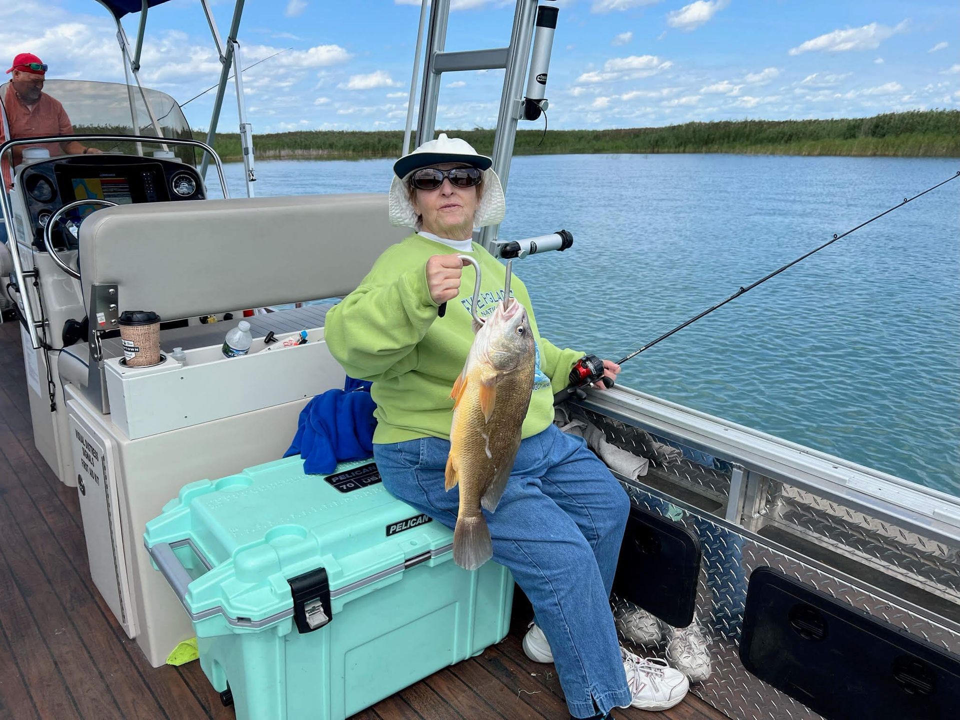 Woman on a pontoon boat holding up a fish; sunny day on the water.