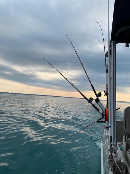 Fishing rods on a boat, overlooking the water with a cloudy sky at dusk.