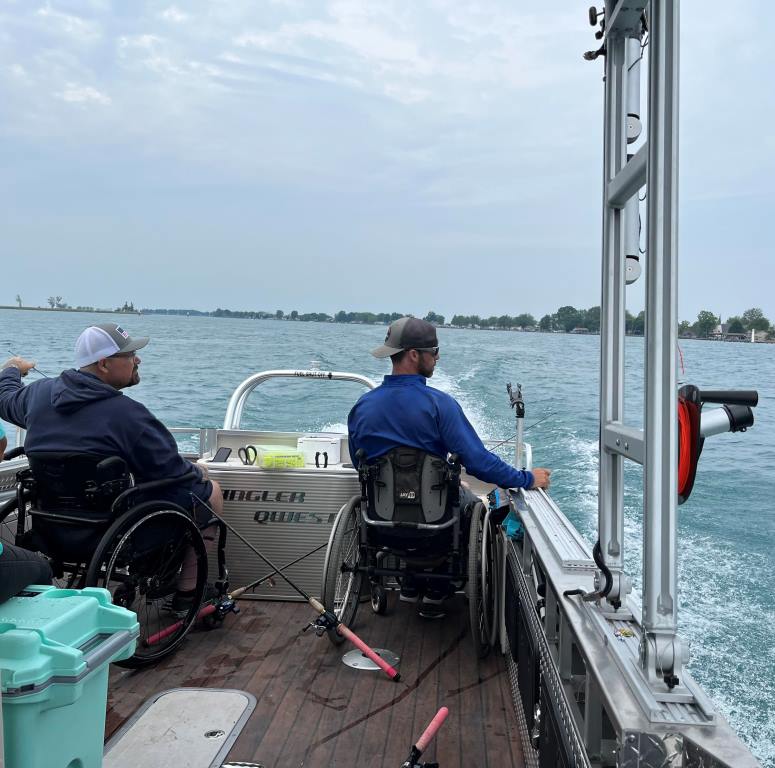 Two people in wheelchairs fishing from a boat on a lake.