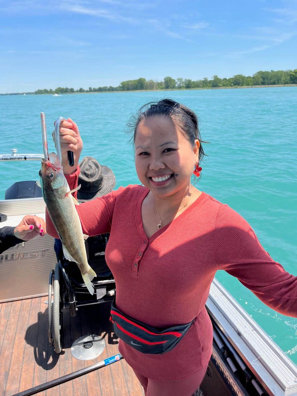 Woman on a boat holding a fish, smiling. Clear blue water and sky in background.