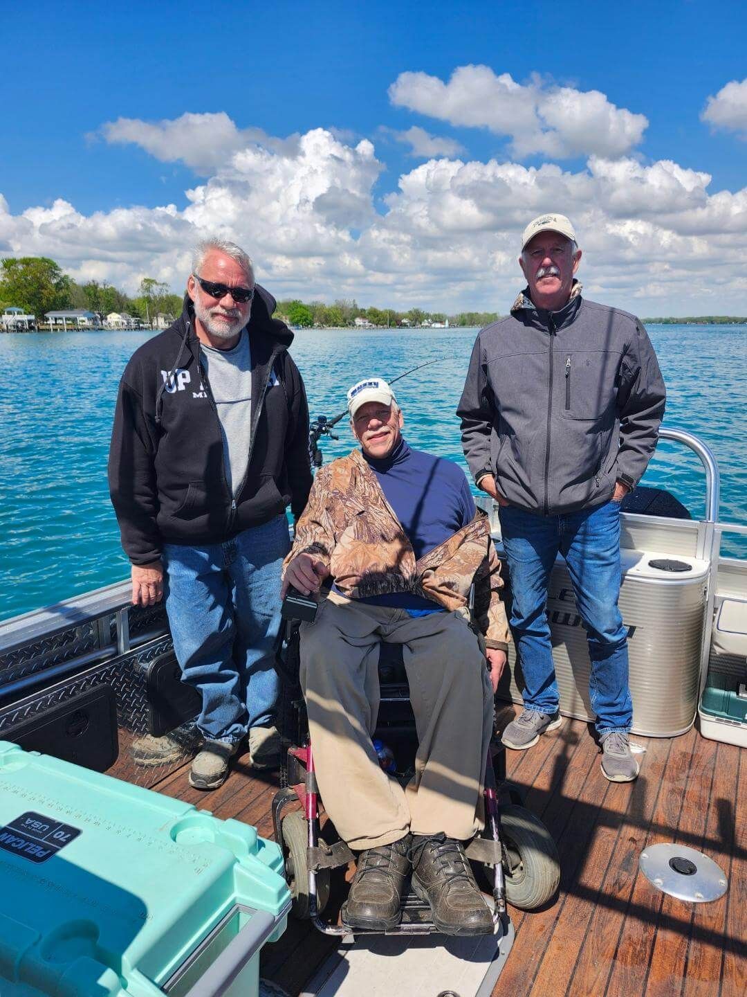 Three men on a boat, one in a wheelchair, on a sunny day.