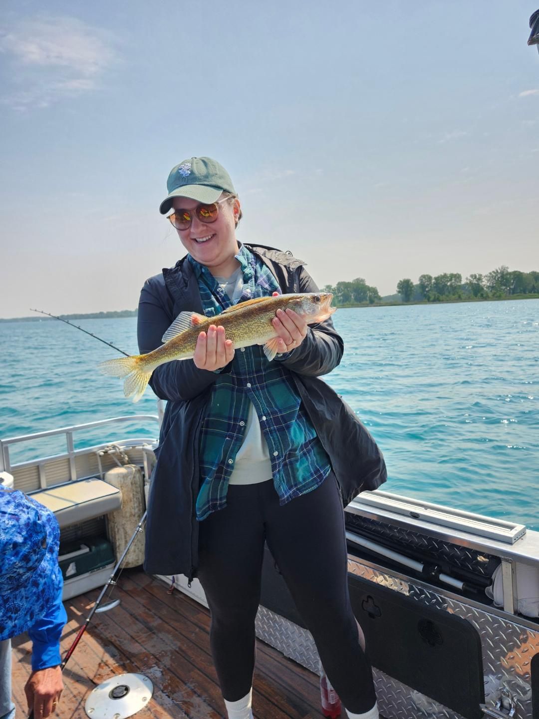 Woman on boat holding a fish, blue water, sunny day.