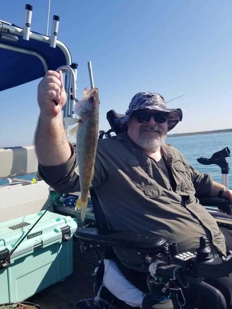Man in a wheelchair on a boat holding a fish up with a fishing hook. Sunny day on the water.