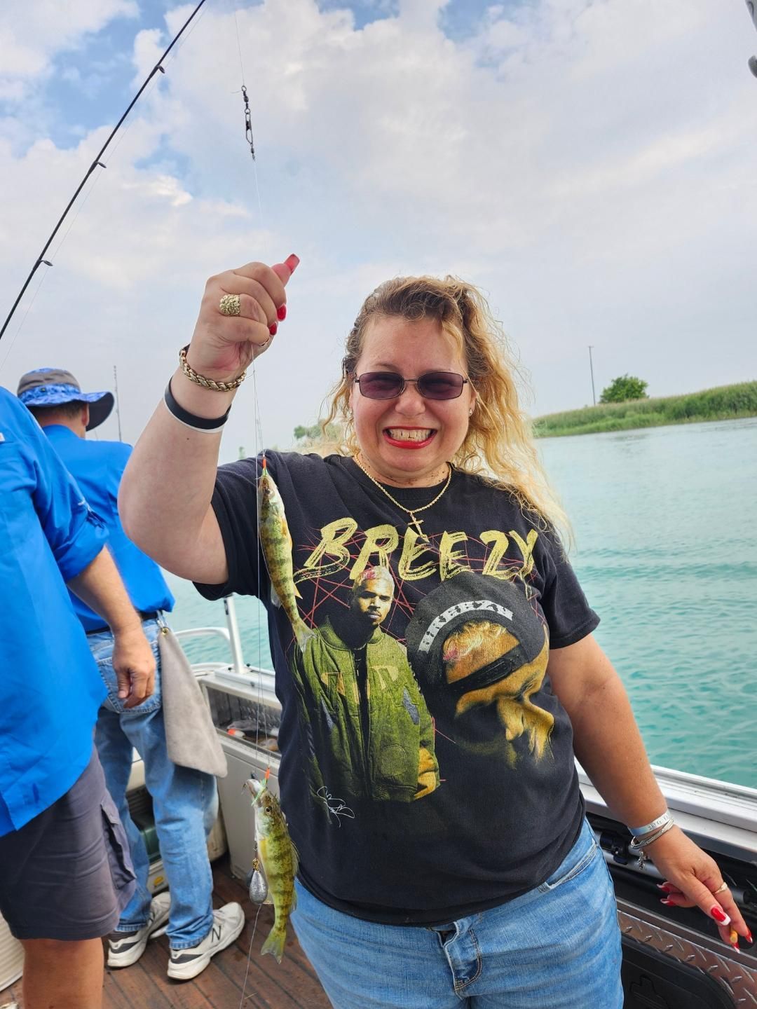 Woman on boat, smiling, holding up two fish. Wearing sunglasses and a 