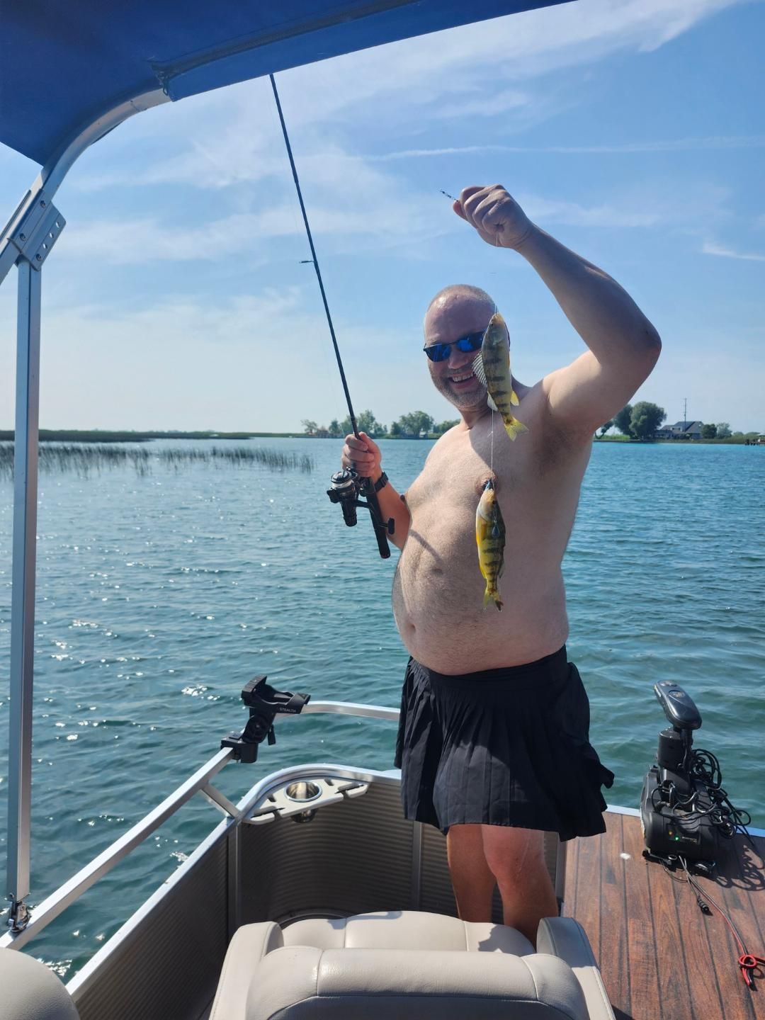 Man on boat holding up two yellow perch; sunny day on lake.