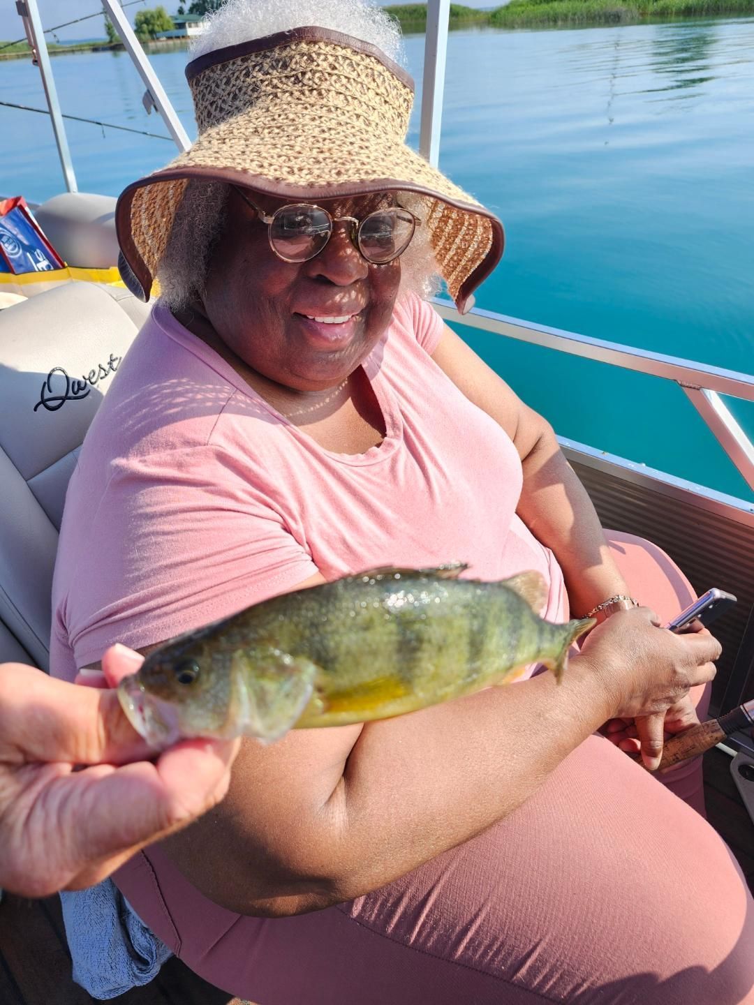 Woman on boat holding a fish, smiling. Sun hat, water background.