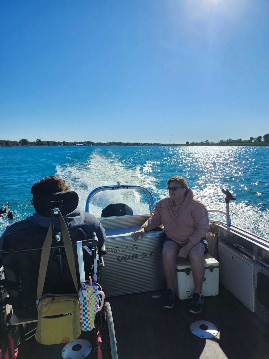 Person in wheelchair and person on boat enjoying a sunny day on the water.