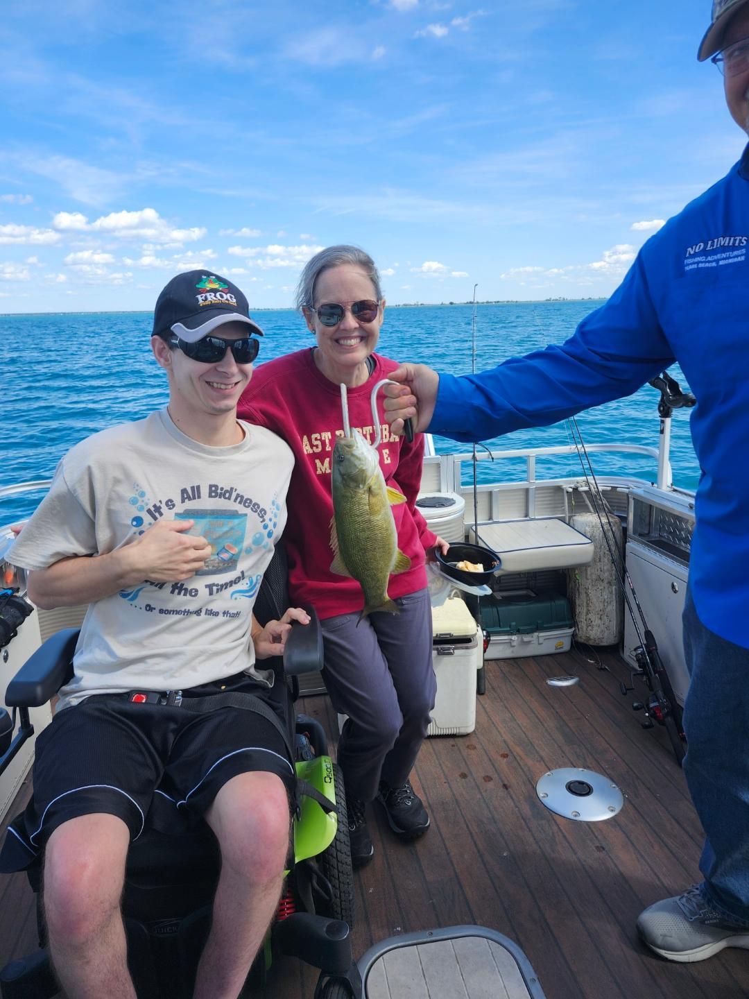 People on a boat with a fish they caught. One person is in a wheelchair. Sunny day, blue water.
