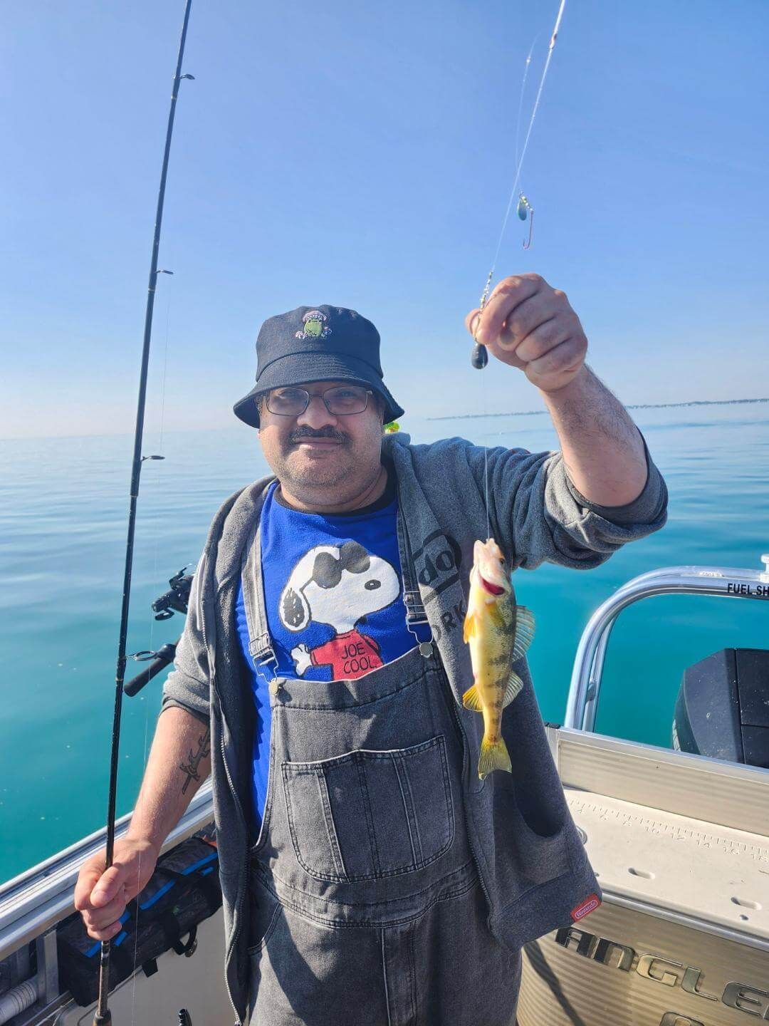 Man on a boat holds up a small yellow fish, blue water and sky in the background.