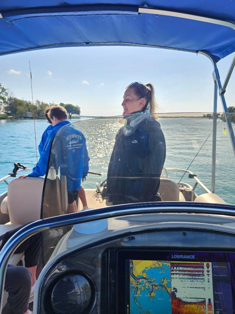 Woman on a pontoon boat, looking towards water. Another person fishing in the background. Bright sunny day.