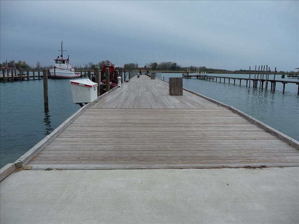 Wooden pier extending into water, boats docked alongside, overcast sky.