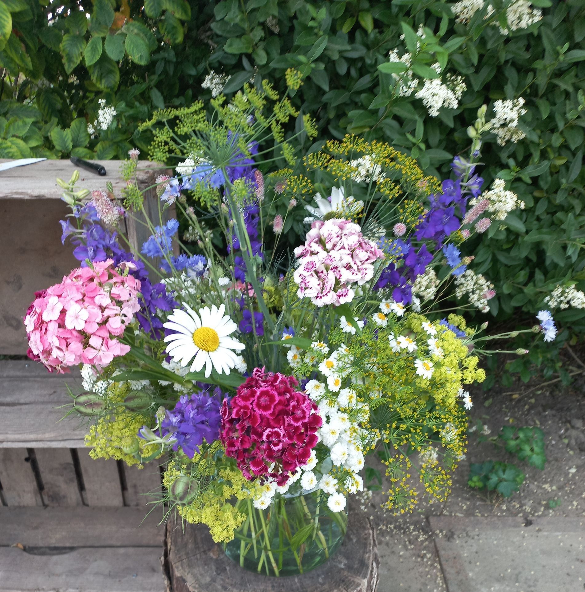 Een kleurrijk boeket bloemen, met roze, paarse, witte en gele bloemen, in een transparante glazen vaas.