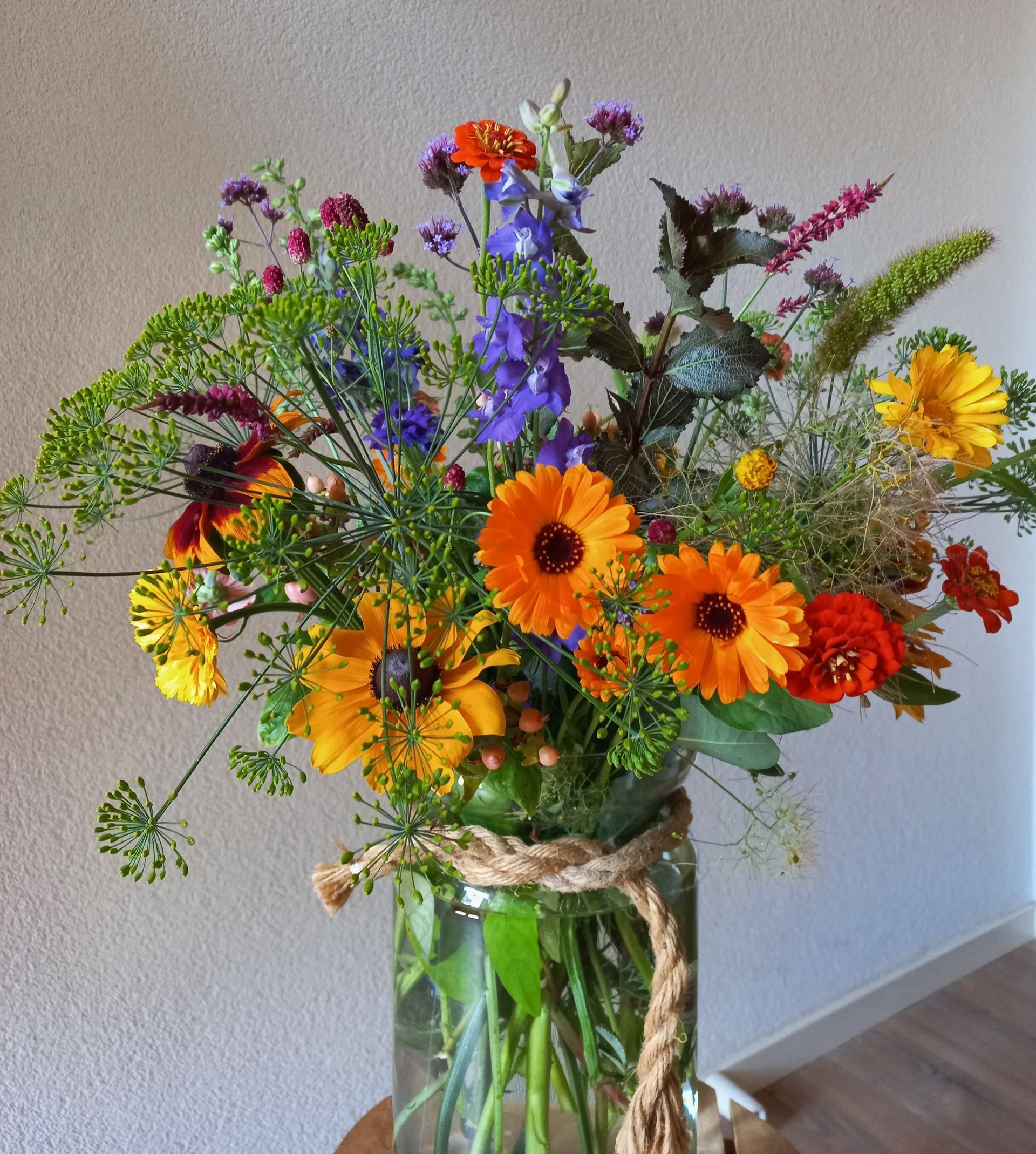 Een kleurrijk boeket van diverse bloemen in een glazen vaas, vastgebonden met touw.