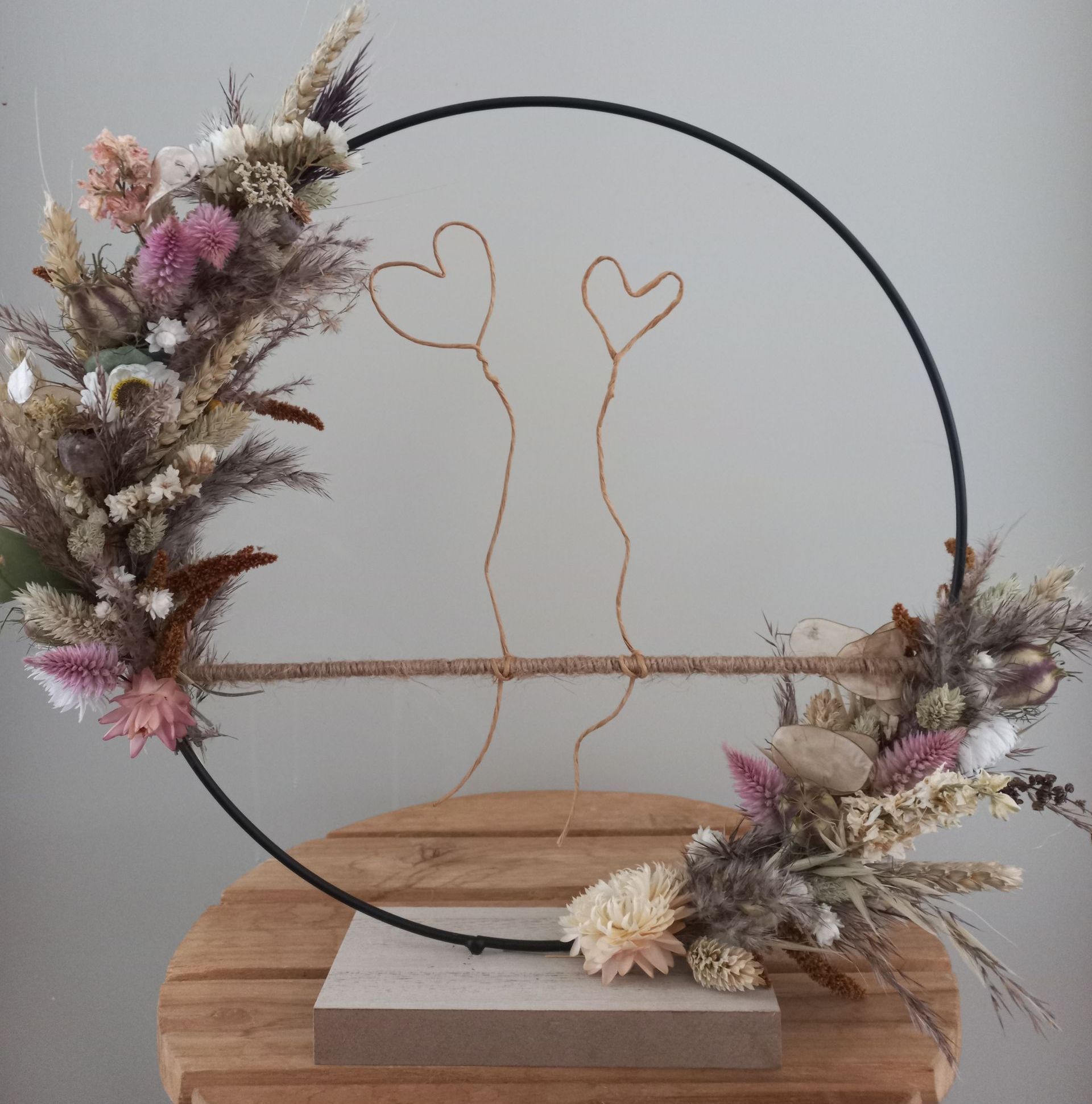 Zwarte ring met gedroogde bloemen en hartjes van koperdraad, op een houten voet.